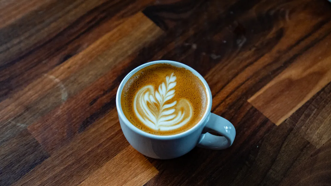 A latte with leaf latte art on a wooden table