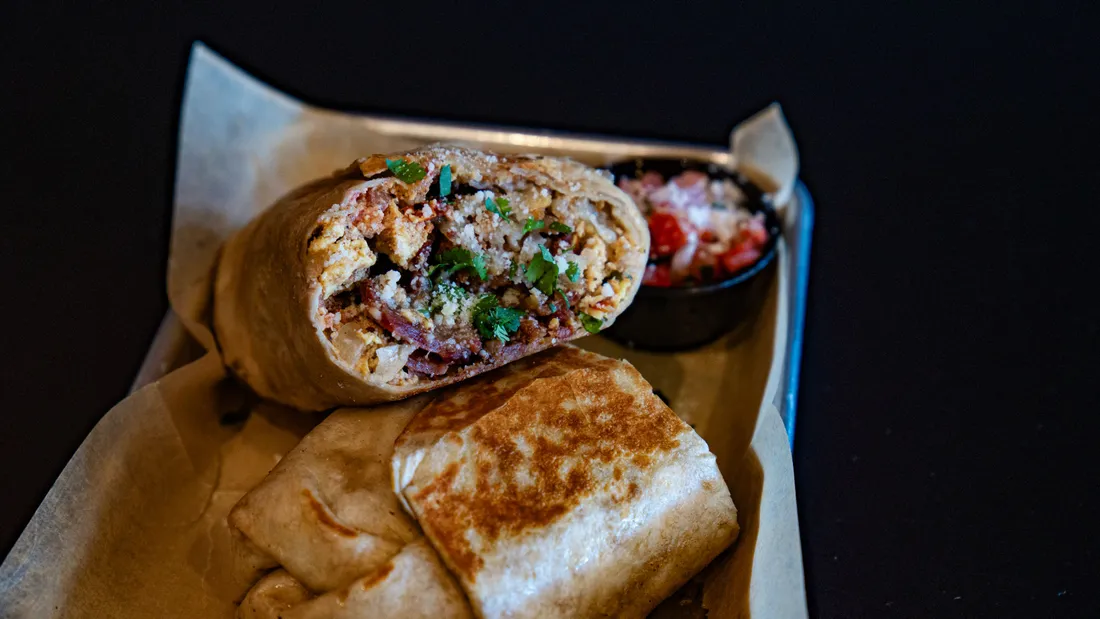 A breakfast burrito cut open, served with a side of fresh salsa